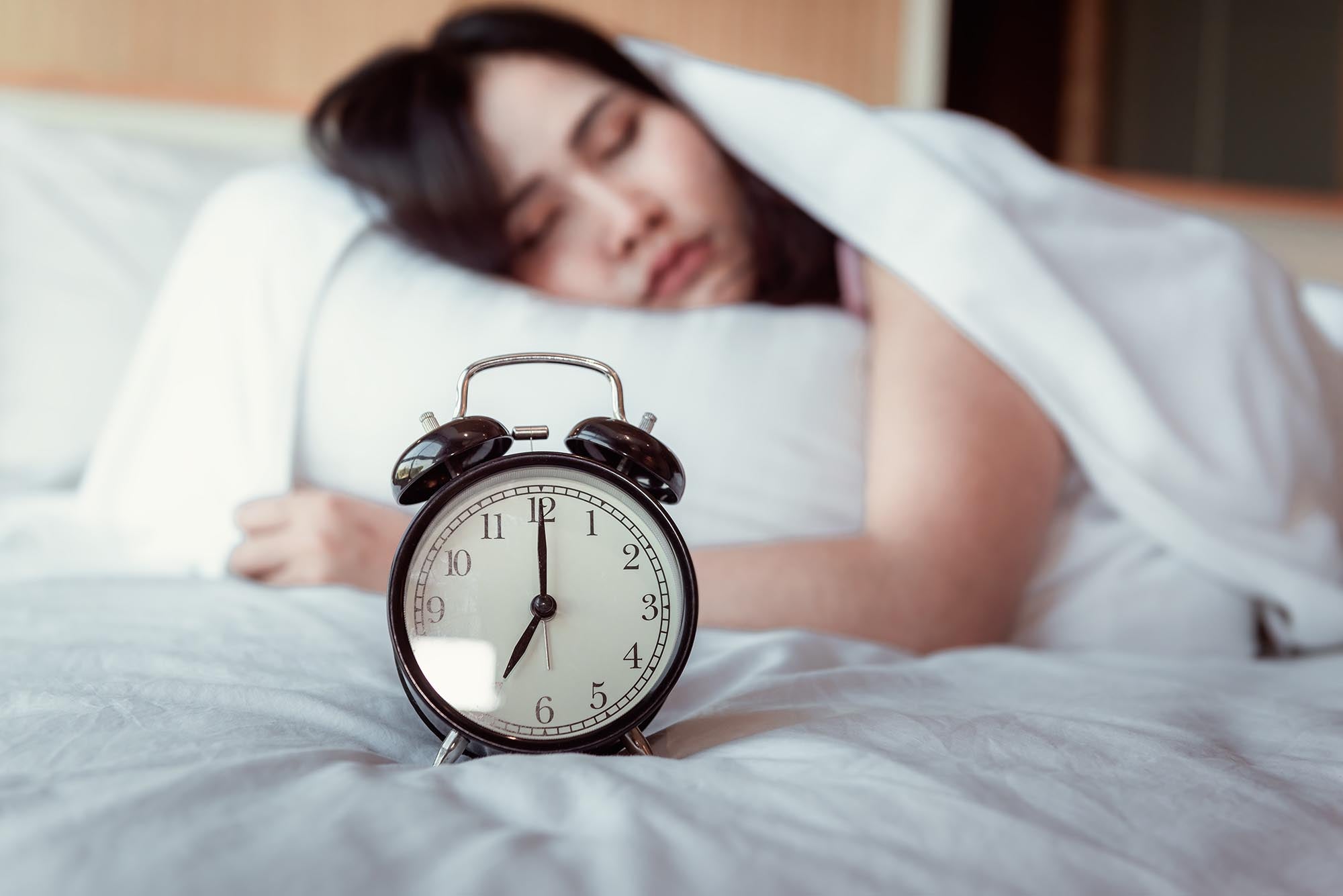 A woman sleeping with an alarm clock beside her, illustrating a moment within her sleep cycle by Magniflex
