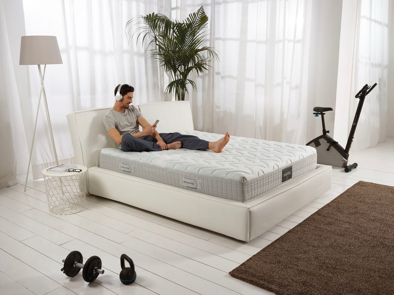 A man comfortably sitting in his Magniflex bed with a spacious vibe, complemented with light accessories.