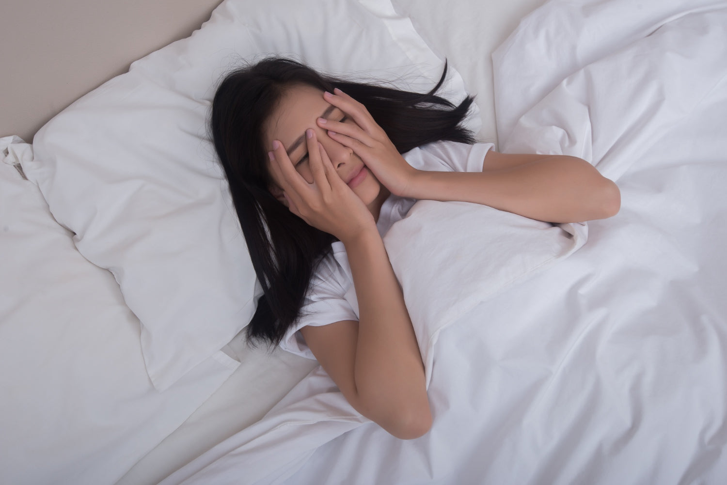 Woman lying on bed covering her eyes due to fear of sleep paralysis.